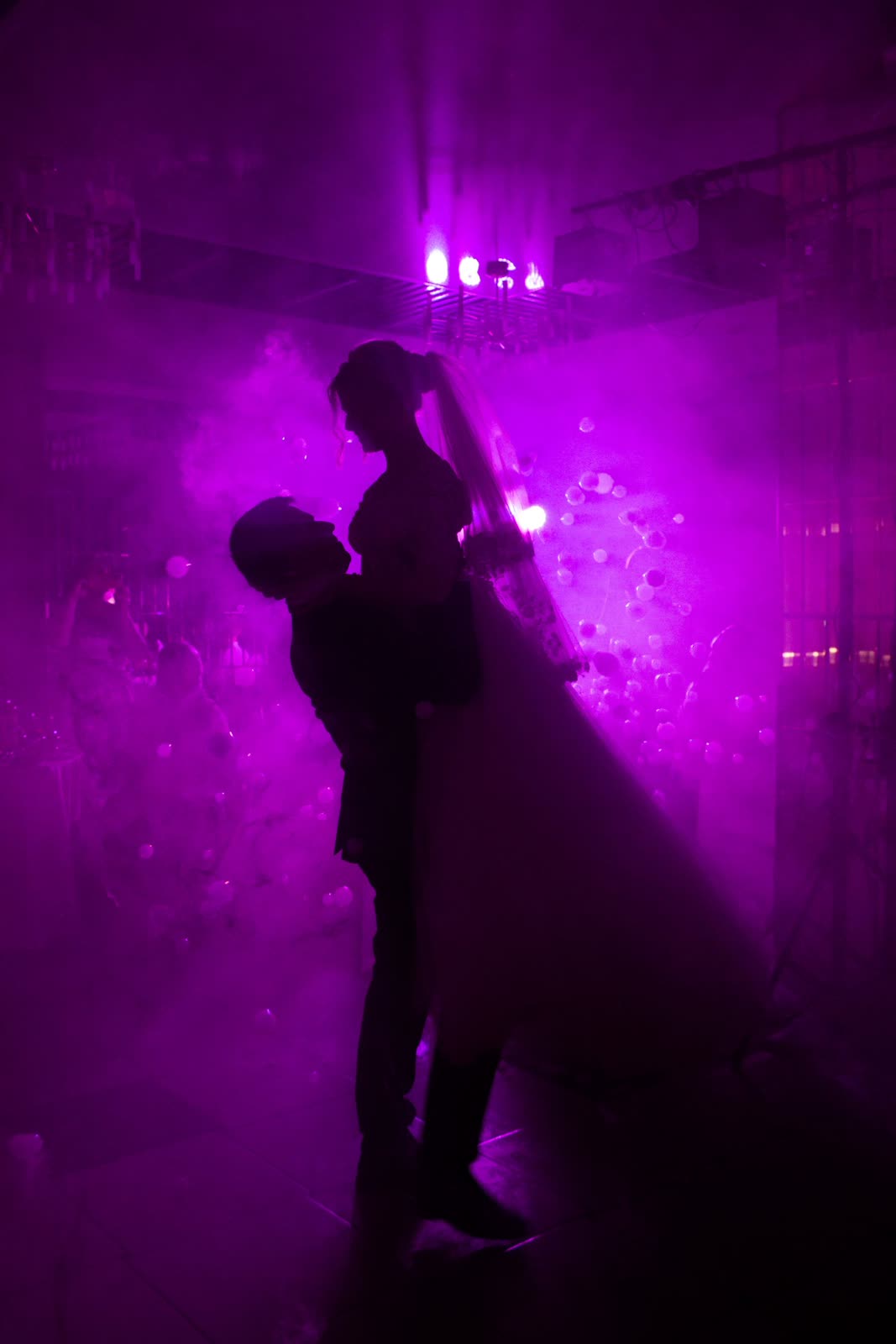 Silhouettes of a groom lifting a bride in purple stage light