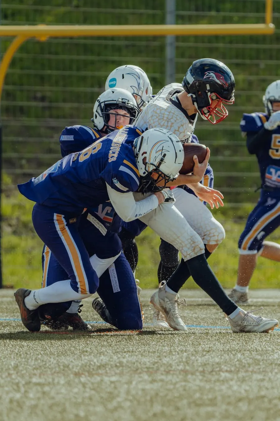 Ein Ballträger der Bucks im blauen Trikot wird von einem Gegner in Weiß zu Boden gerissen.