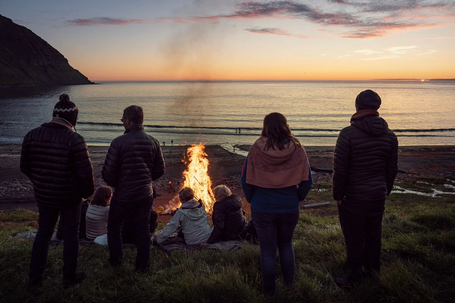 Group watching a bonfire by the sea during a calm sunset.