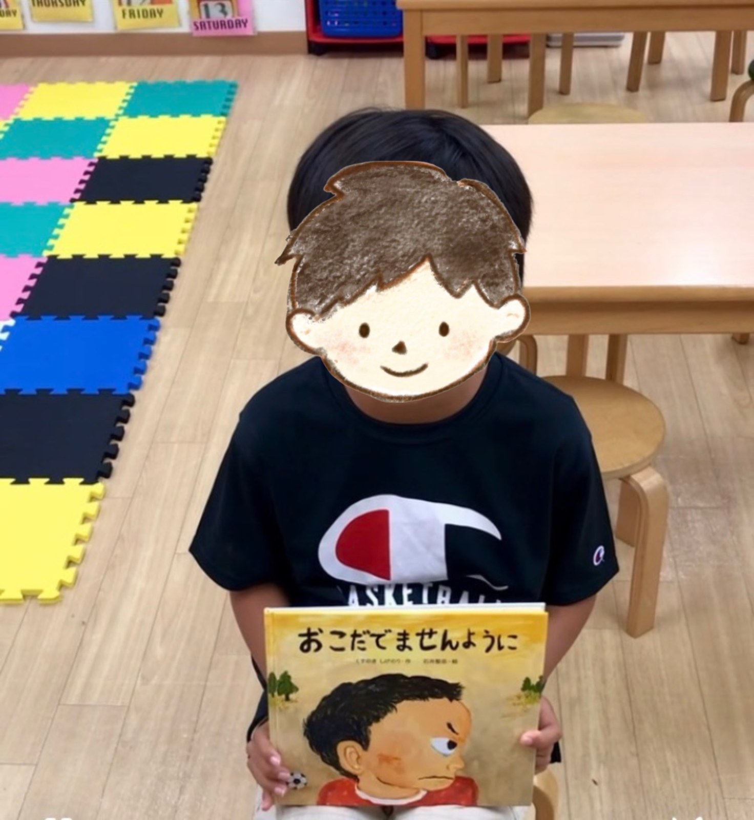 絵本『おこだでませんように』を持って発表する子ども（顔はイラストで隠しています）