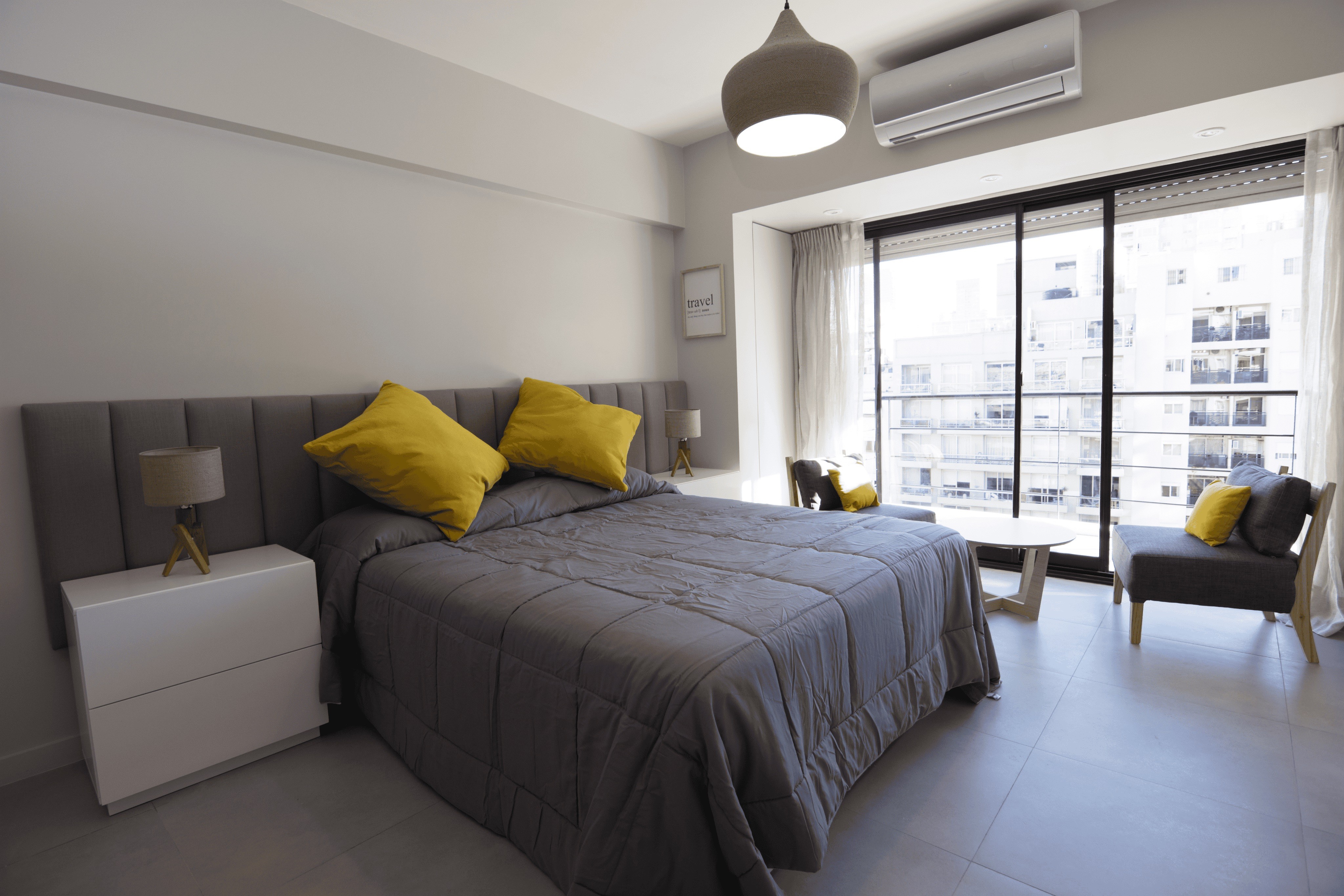 Modern bedroom with a grey comforter, yellow pillows, and a balcony view.