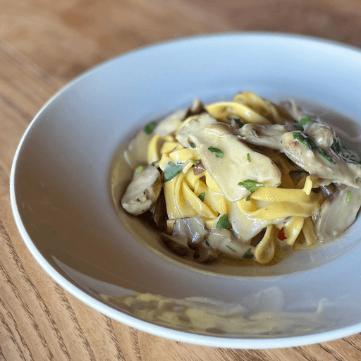 Plate of creamy tagliolini pasta topped with abalone mushrooms and grated parmigiano.