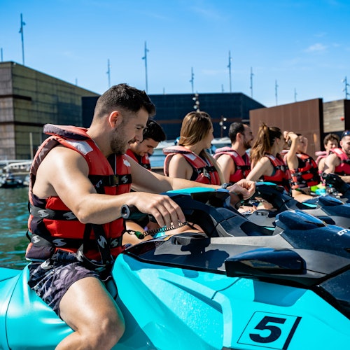 一群人穿著救生衣，坐在碧藍的水上摩托車上，等待在陽光明媚的碼頭出發。