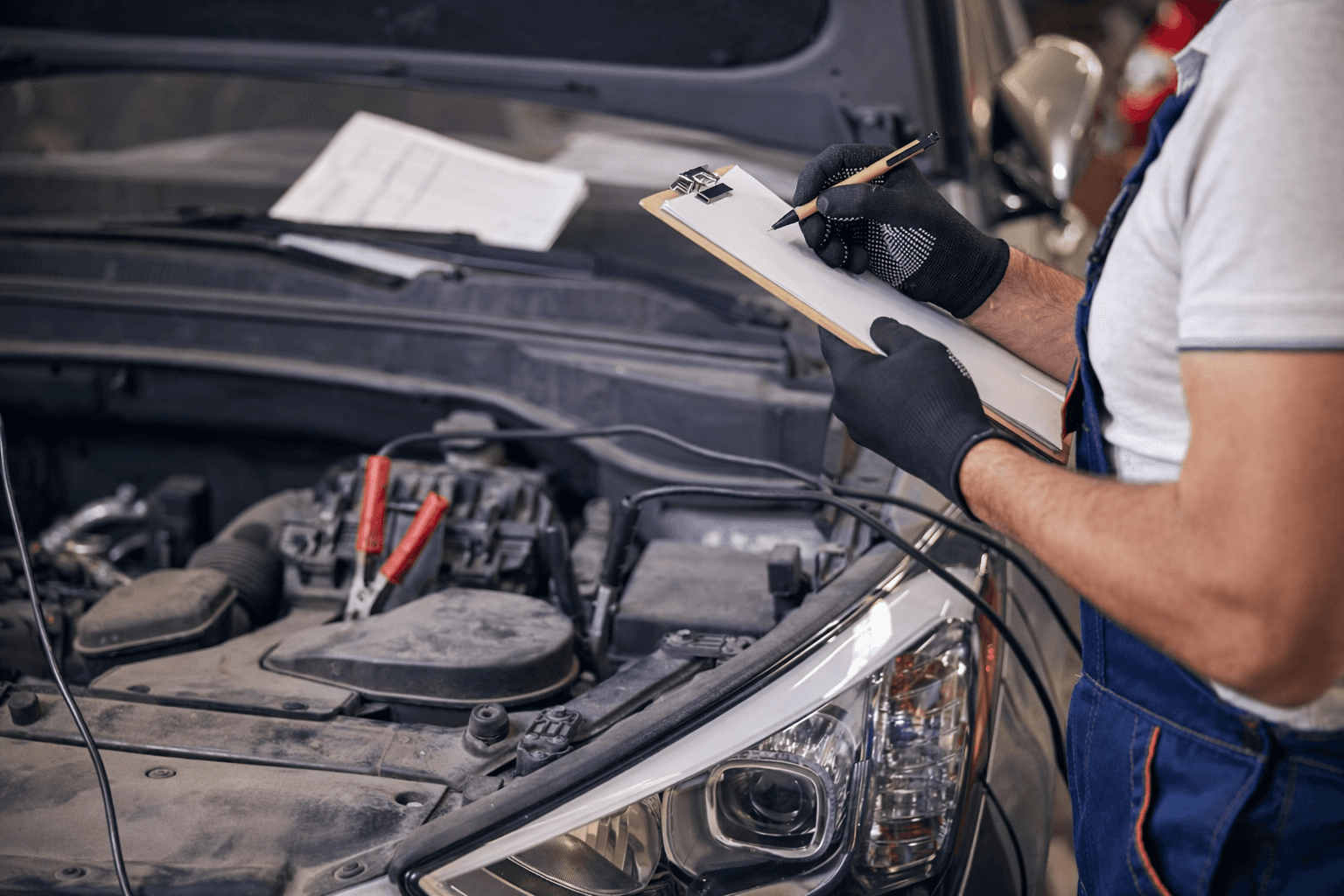 A close-up of a service inspection in progress: the engine bay is exposed while the technician documents findings, like an estimate or repair record.