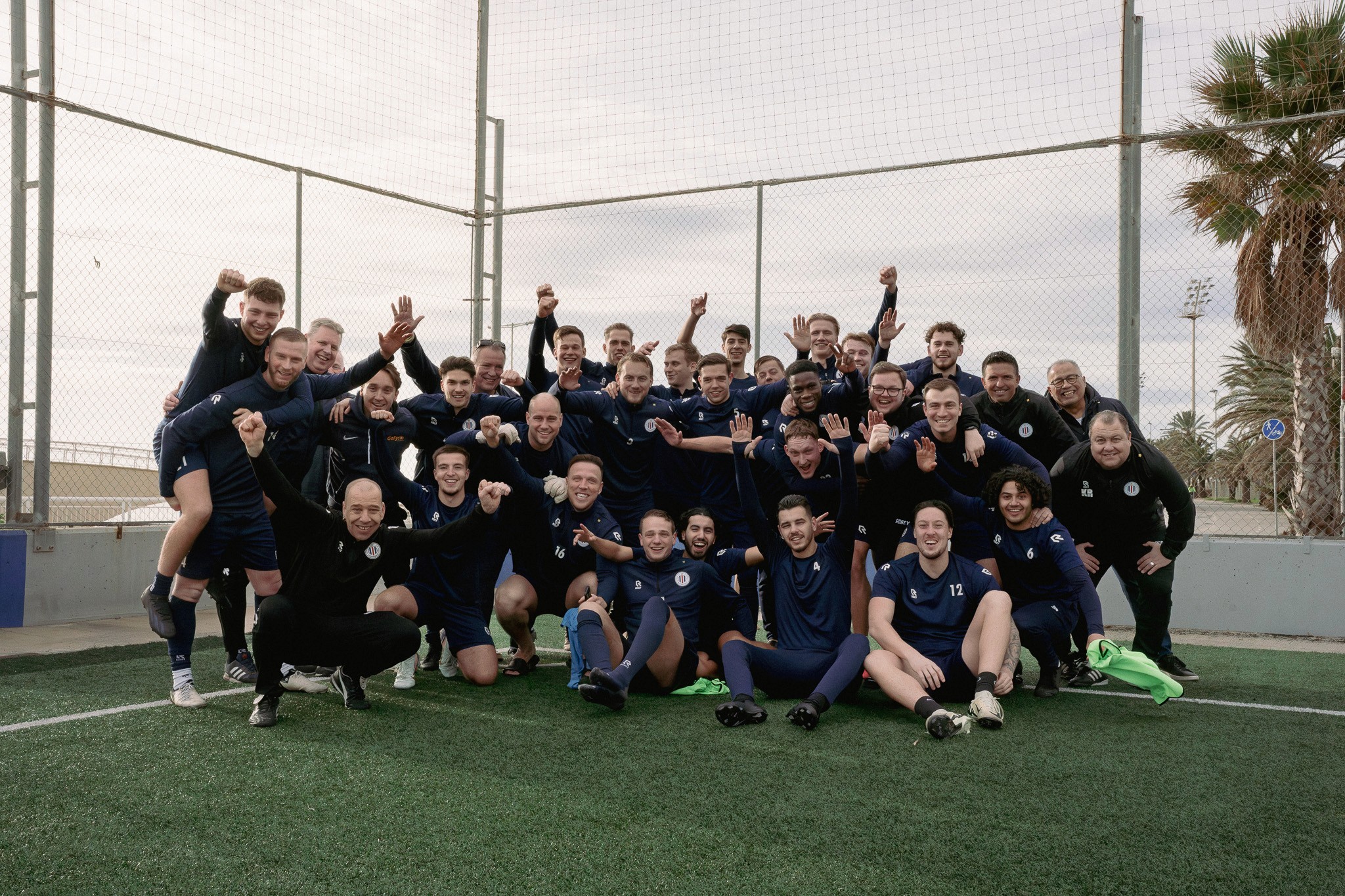Een energieke groepsfoto van een voetbalteam tijdens een training op een prachtig veld aan het strand in Barcelona.