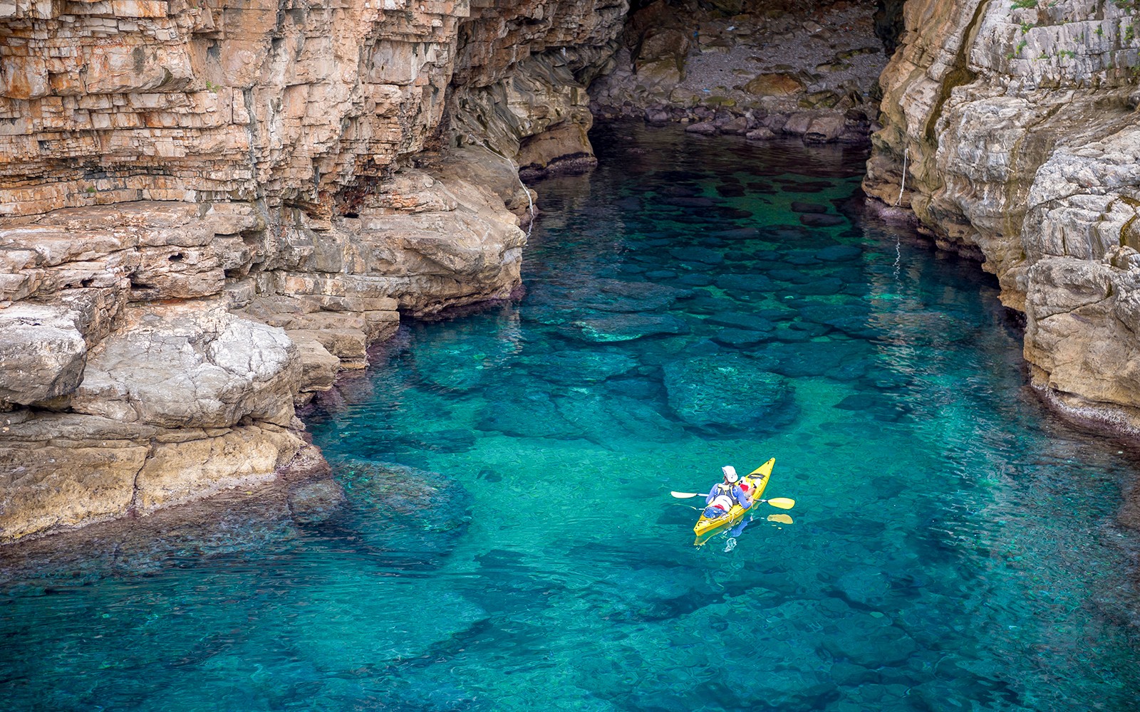 Kayakers exploring Betina Cave's clear waters at sunset.