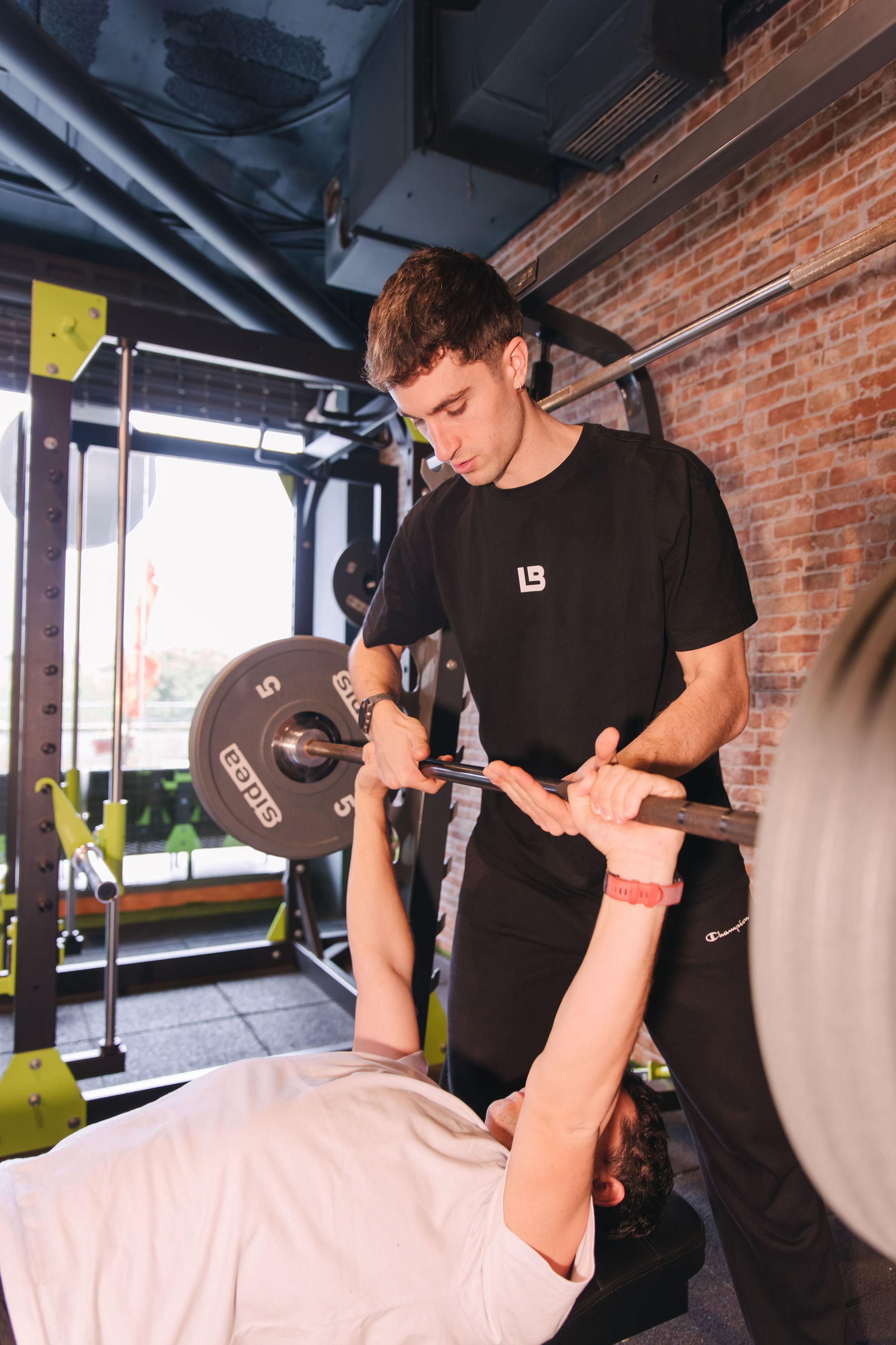 Cliente realizando ejercicio en press de banca con supervisión de entrenador en La Base Strength, Sitges