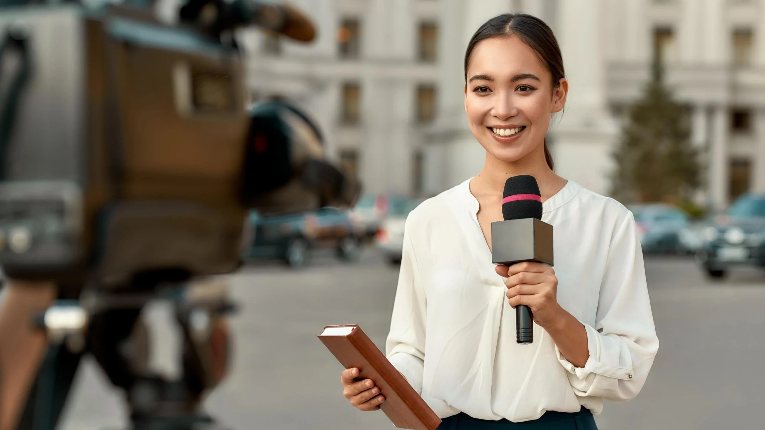 High school students exploring journalism and media careers through RISE Research summer programs; young reporter holds microphone and notebook during urban news shoot.