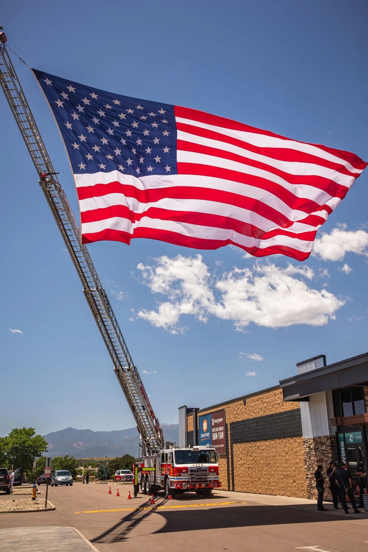 A large American flag waves from a tall flagpole against a blue sky with a few clouds.