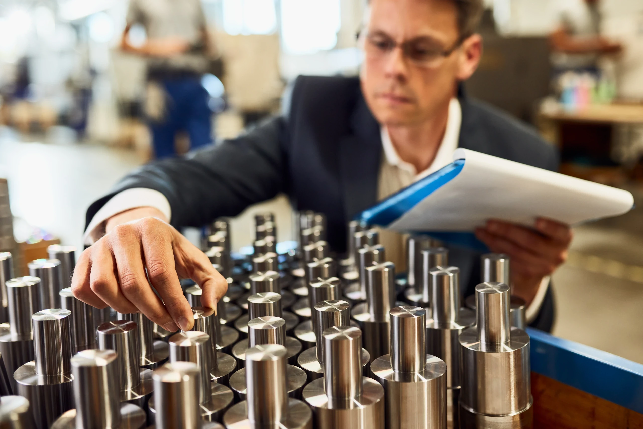 Quality engineer inspecting machined metal parts with a tablet in hand.