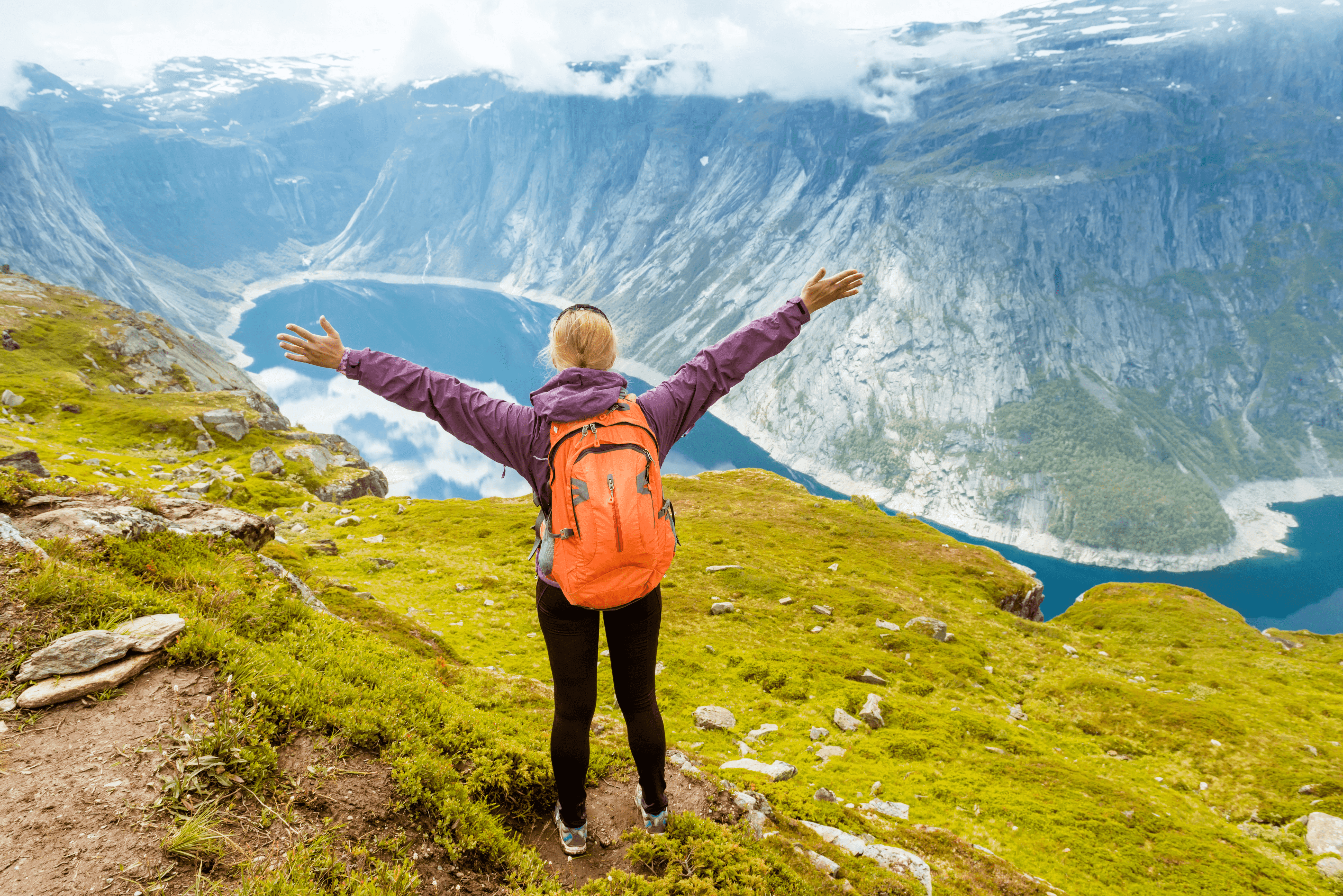woman standing in the mountains with her arms overhead, looking down at a lake