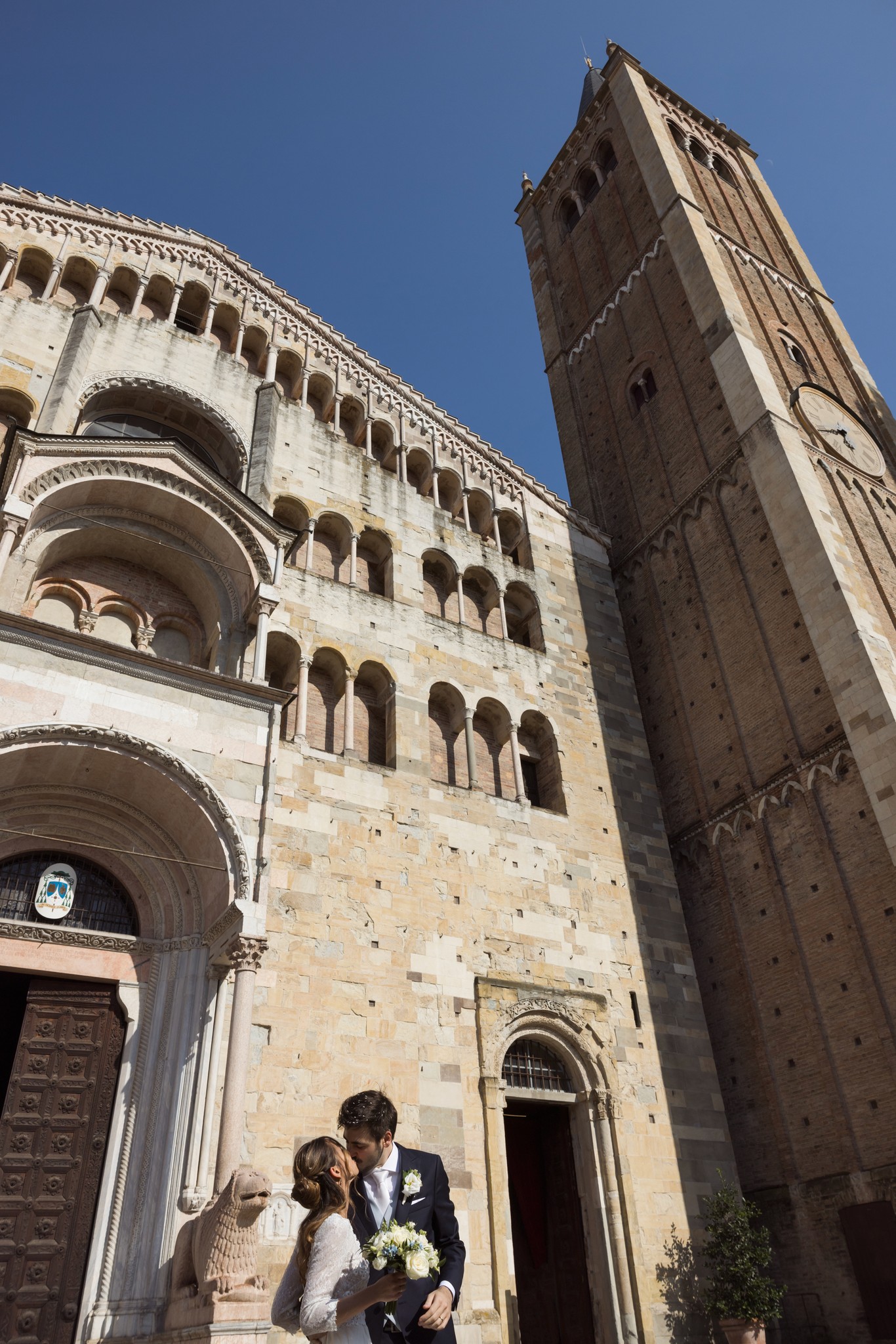 Sposi davanti alla Cattedrale di Ferrara, lui solleva lei tra le braccia al portale romanico, cielo azzurro, matrimonio
