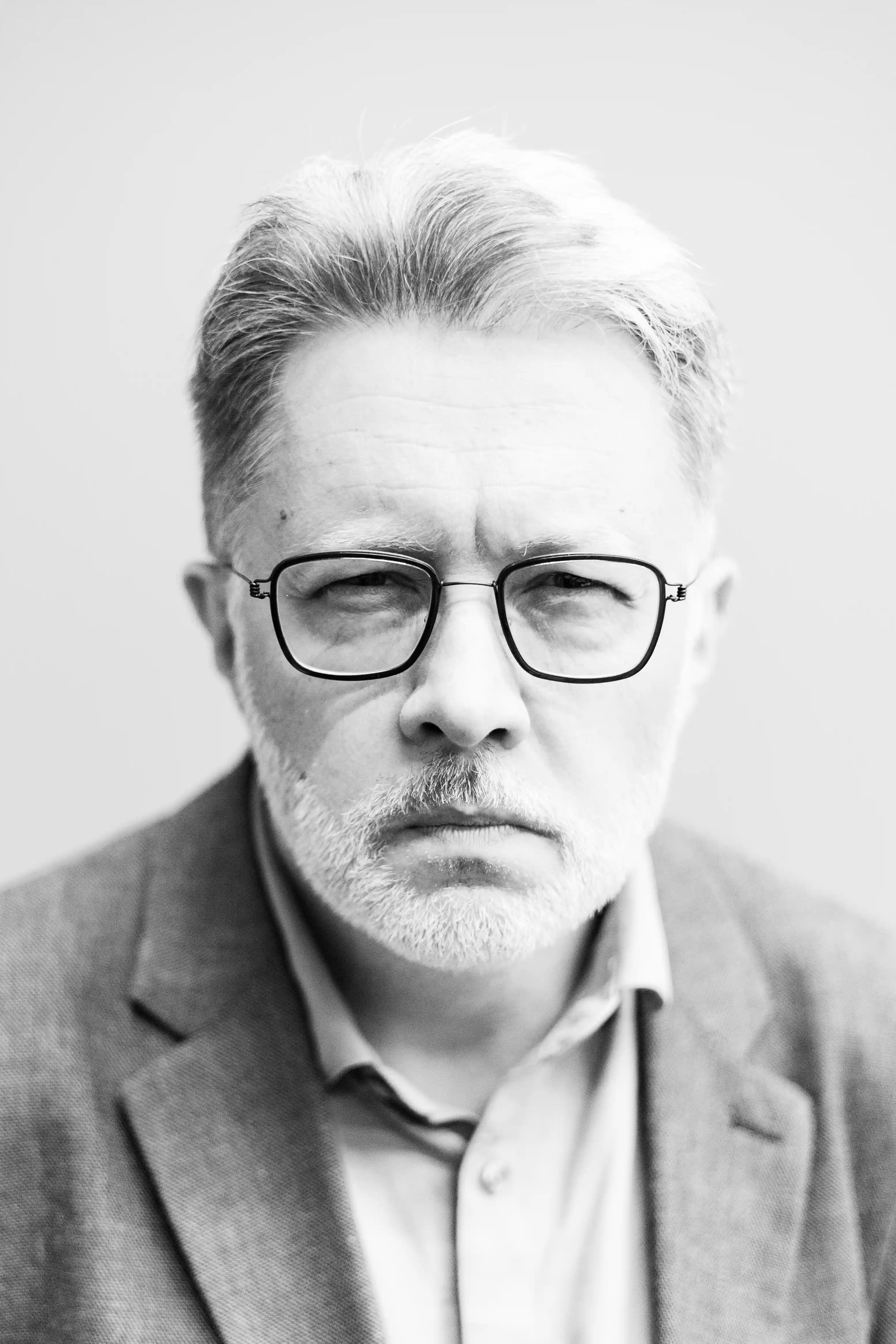 Mężczyzna w średnim wieku w okularach patrzący z poważną miną. Portret na jasnym tle, mężczyzna ubrany jest w garnitur.