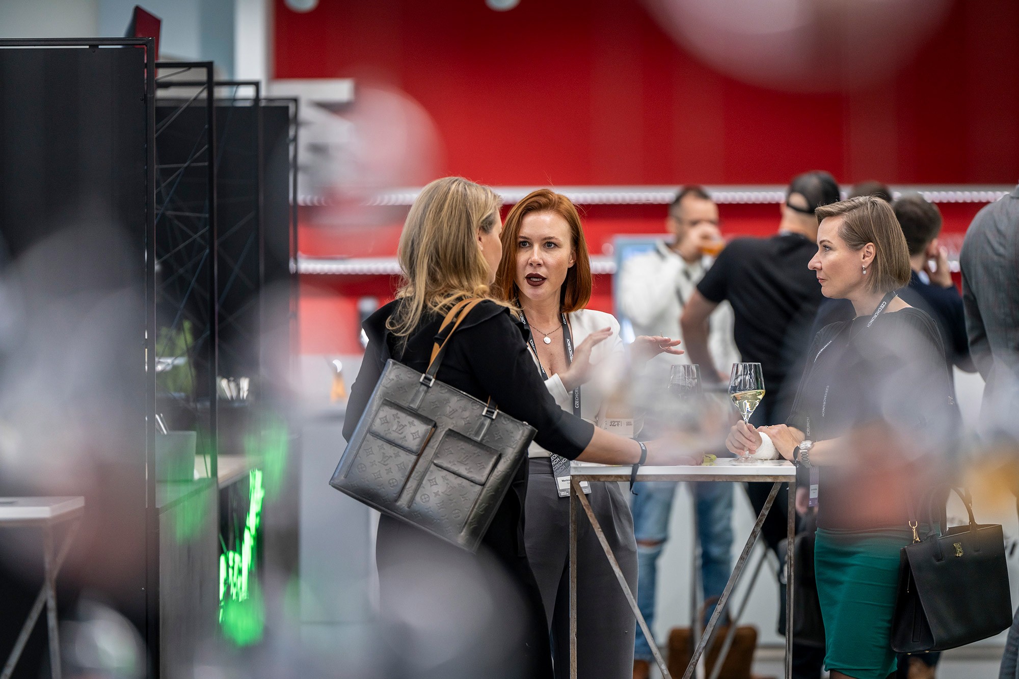 Attendees networking during Money Maker conference by CzechCrunch in Prague, informal discussion at a high table with wine glasses.