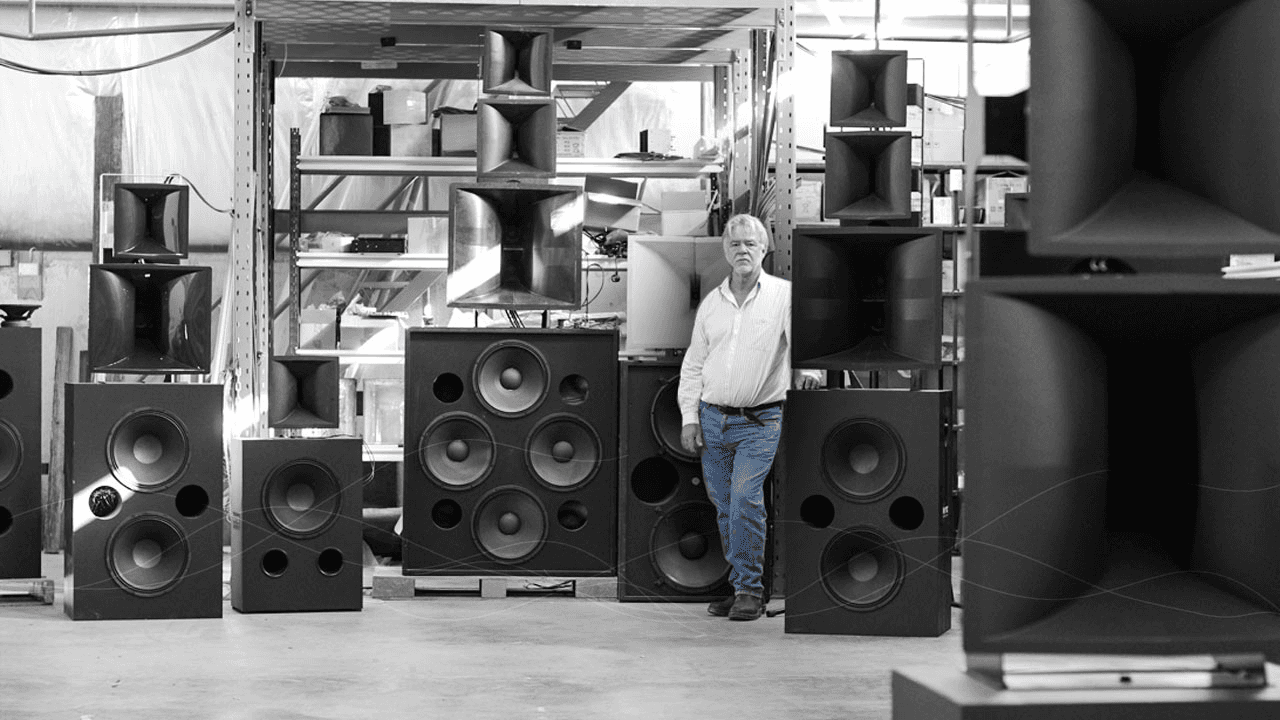 Man standing amongst large horn speakers and subwoofers.