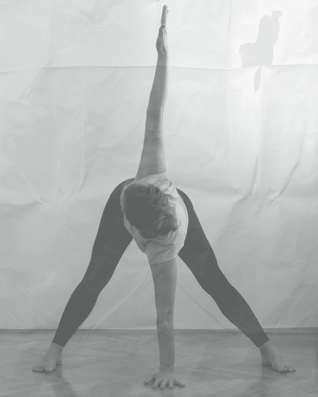 A grayscale image of a person performing a yoga pose with legs spread wide and one arm extended upwards.