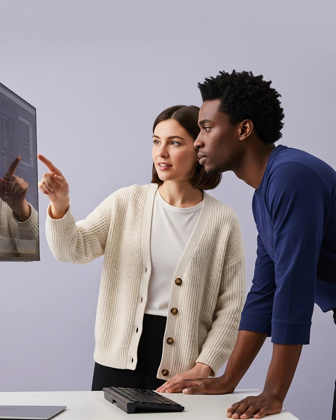 Two colleagues work together at a desk, concentrating on a computer screen in a modern office.