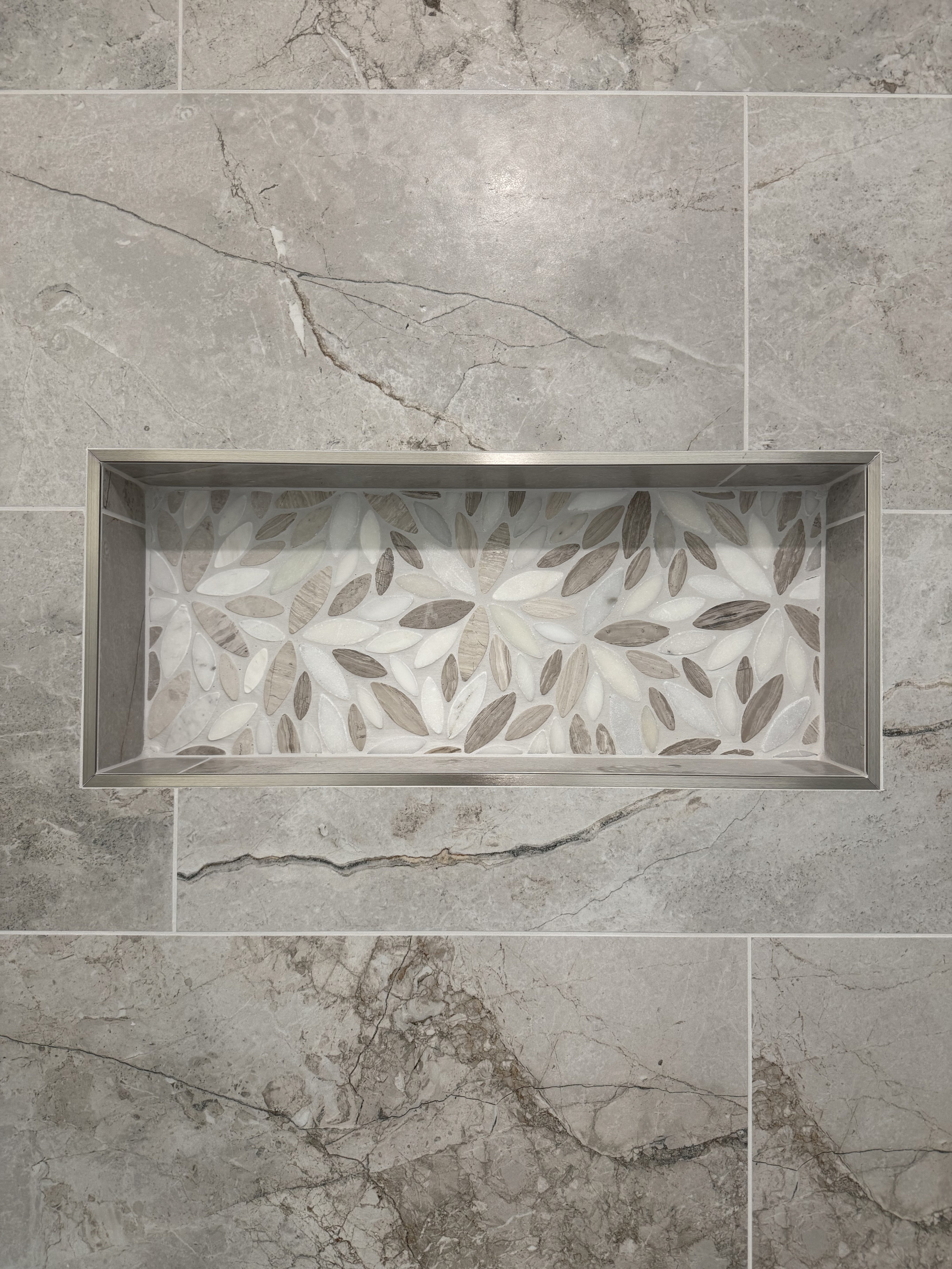 Bathtub shower combo with sleek grey marble-look large format wall tiles, a built-in shower niche with a white and grey hexagonal mosaic tile accent, and modern chrome fixtures.