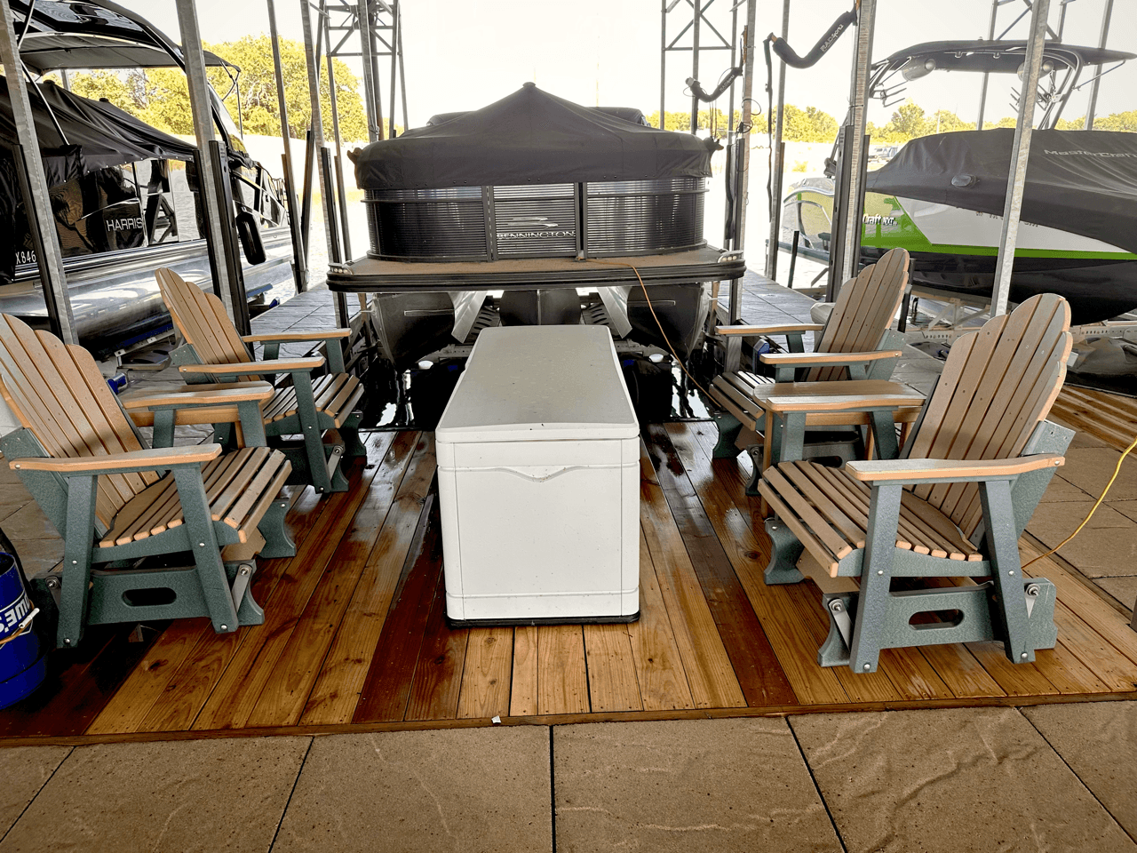 Several wooden chairs arranged around a white chest on a docked pontoon boat, surrounded by other boats in a marina under a clear sky.