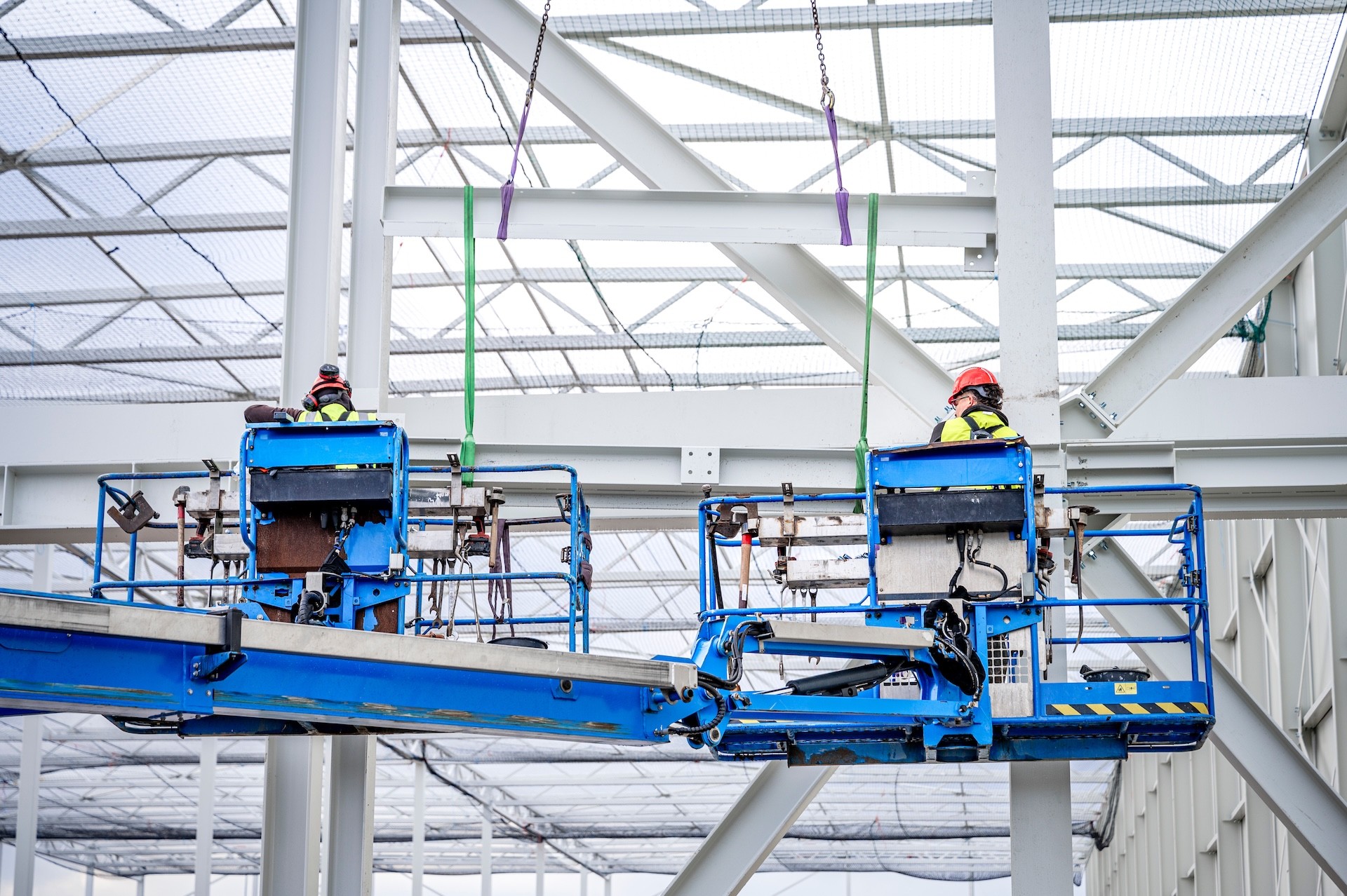 Blauwe hoogwerker met montagemedewerkers werkend aan staalconstructie