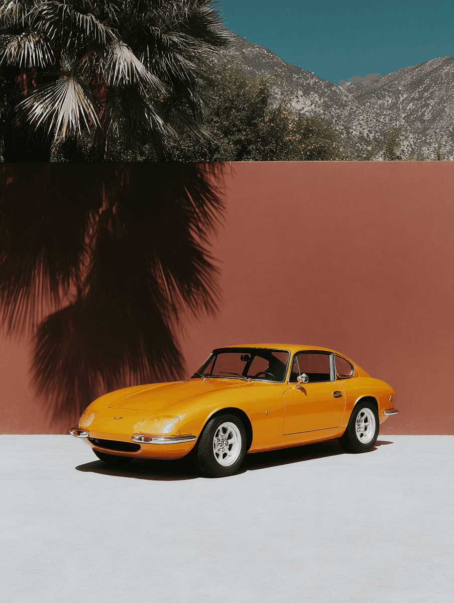 A bright yellow car parked against a pink wall, with palm trees and mountains in the background.