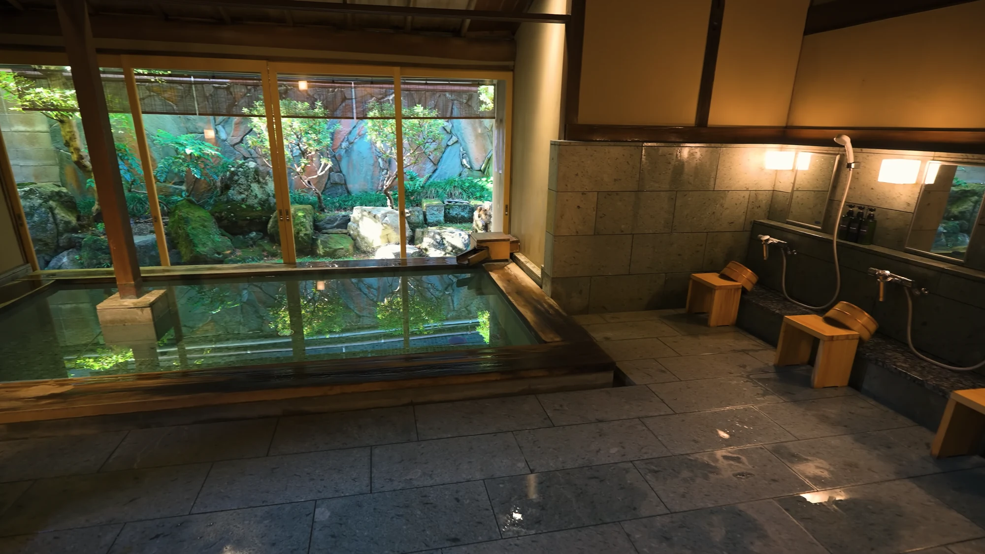 Washing stations with stools and taps along the wall of a Kinosaki public bath.