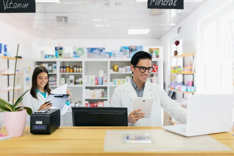 ai pharmacy demonstrated by pharmacists using a tablet and laptop to manage prescriptions and inventory at a pharmacy counter.