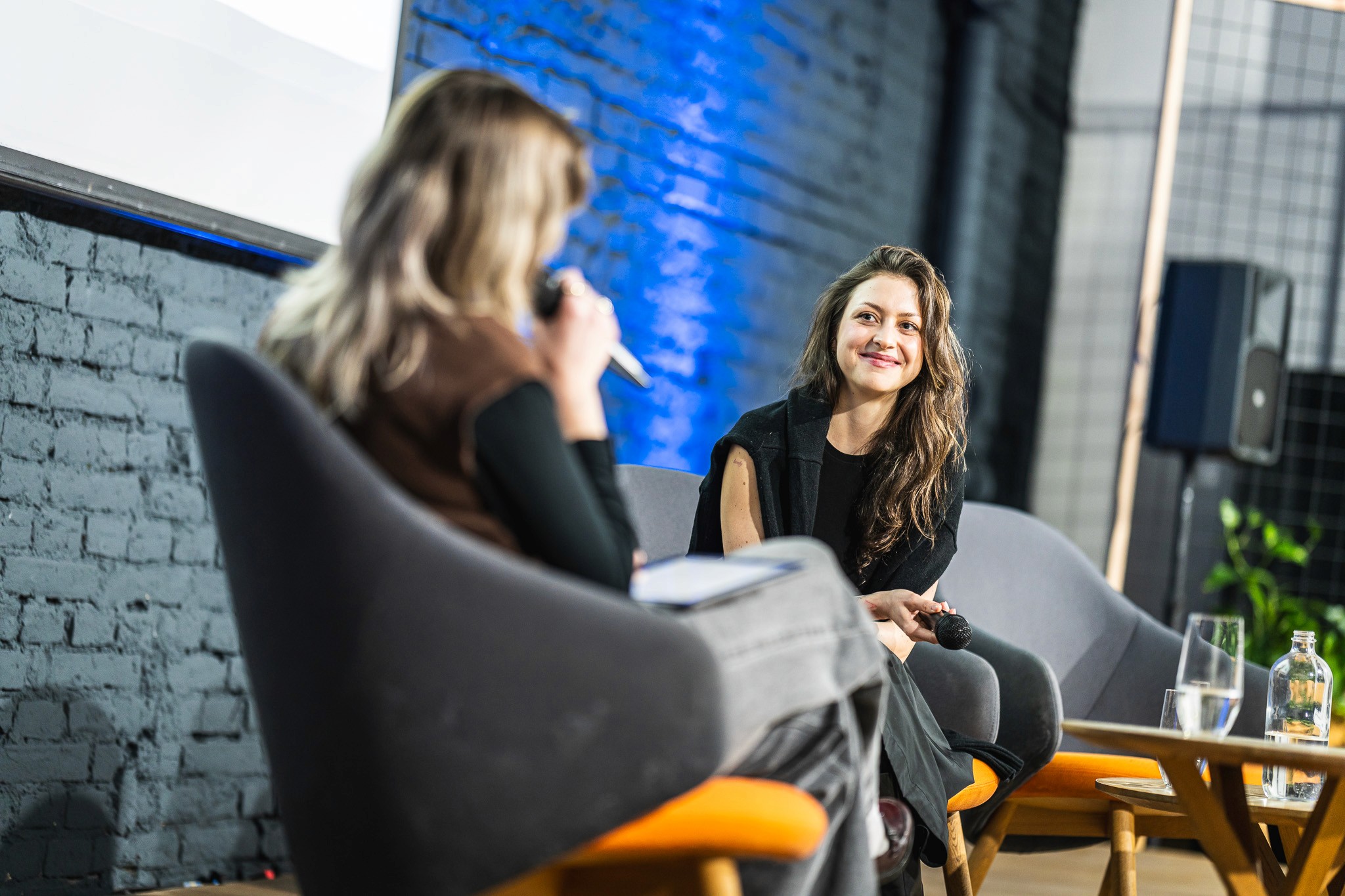 Interview conversation captured during a conference session with seated participants.