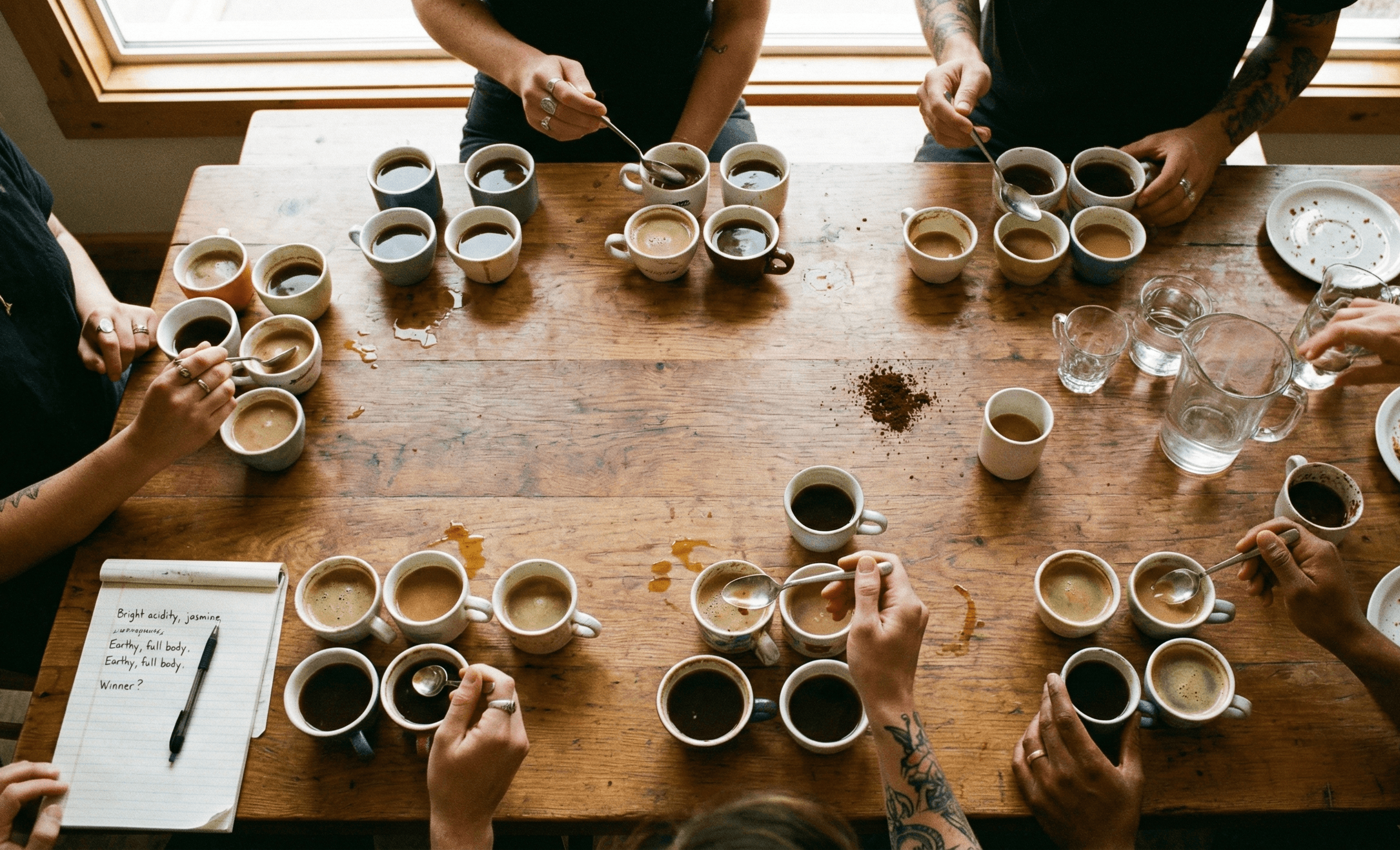 Friends reaching for coffee cups with spoons during a casual coffee tasting party with tasting notes on the table