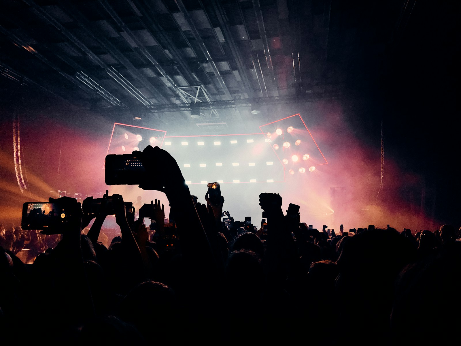 A concert crowd gathered around a stage in blue light