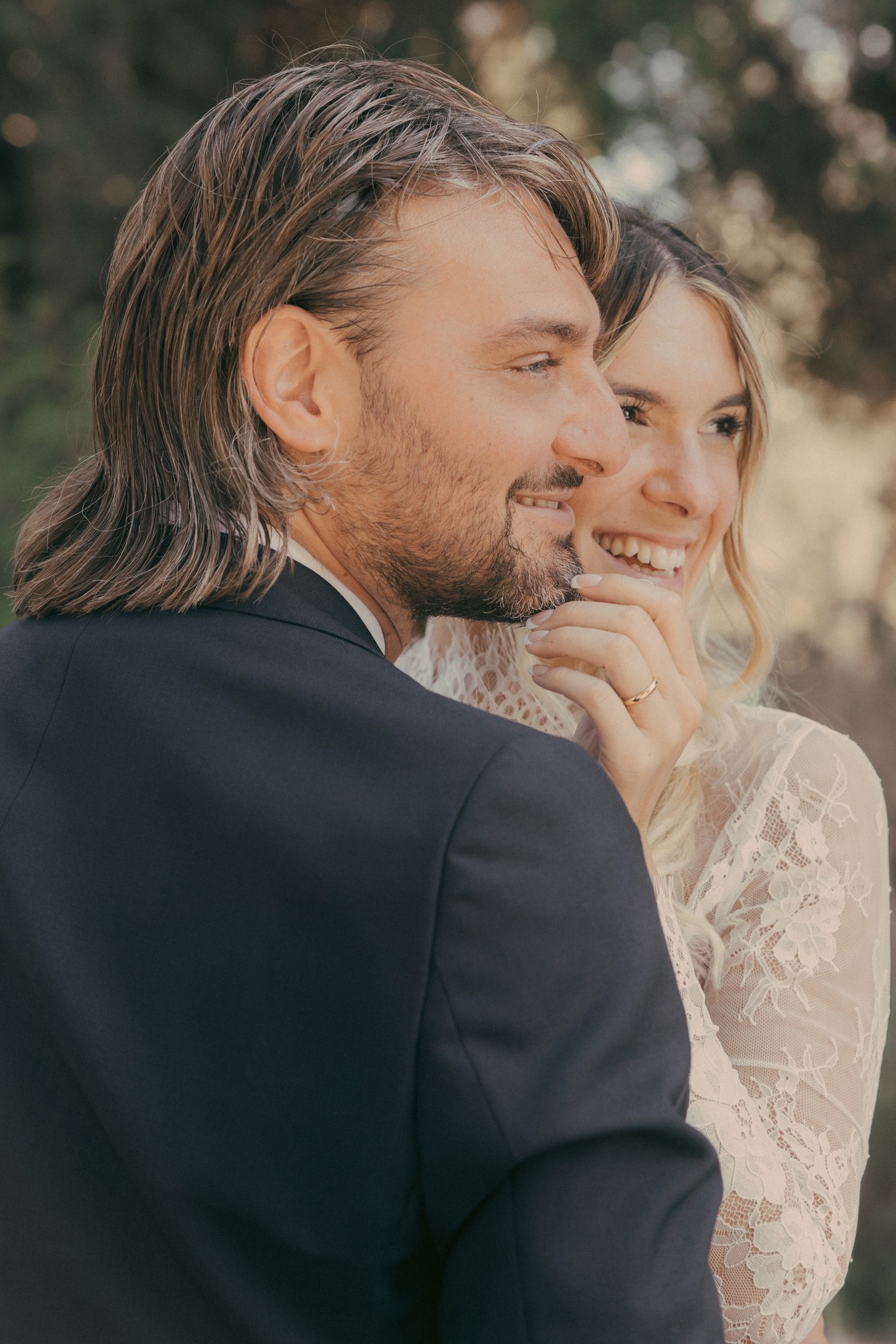 Sposi sorridenti a Bolgheri, lui di spalle in smoking, lei in velo e pizzo, luce autunnale nel reportage matrimoniale