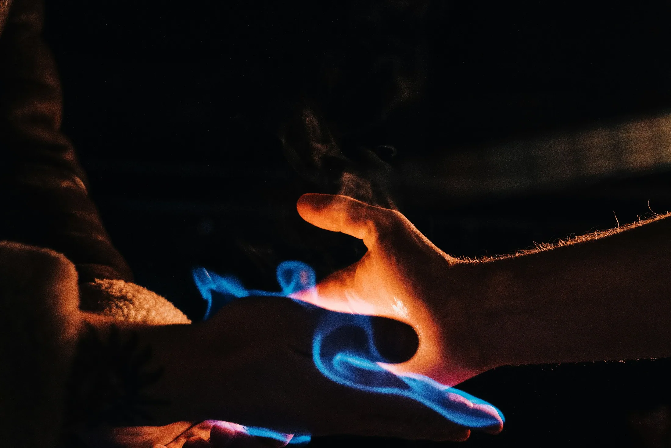Two hands holding blue and orange flames in the dark