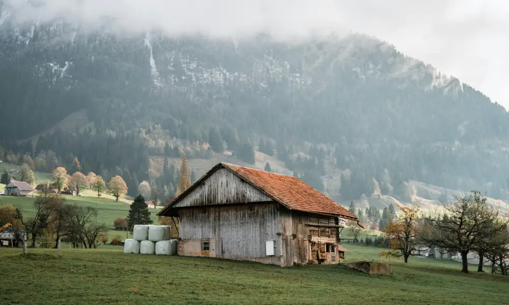 Scheune im Winter mit Heuballen auf Feld vor nebelverhangenem Berg.