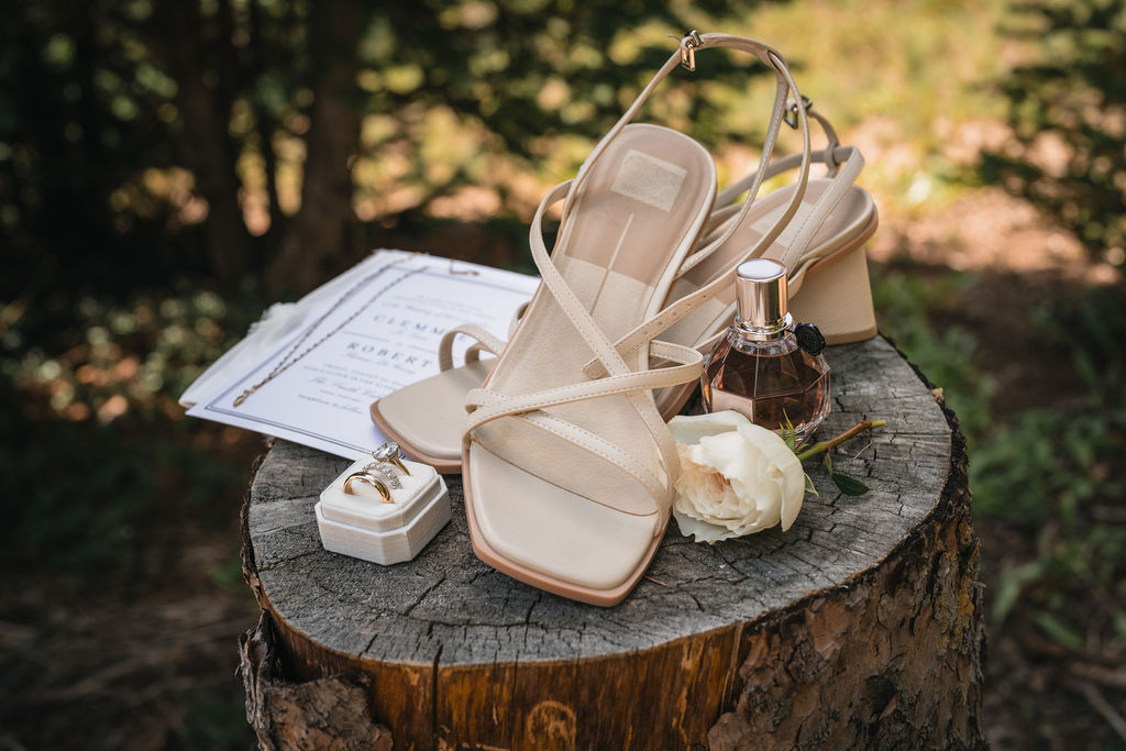 Wedding shoes, jewelry, perfume, and stationery on a tree stump