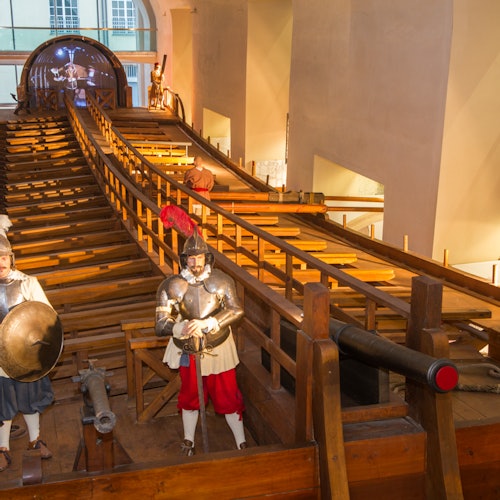 温かみのある照明が施された歴史博物館の展示には、甲冑を身にまとったマネキン、大きな木造構造物、そして大砲が含まれています。