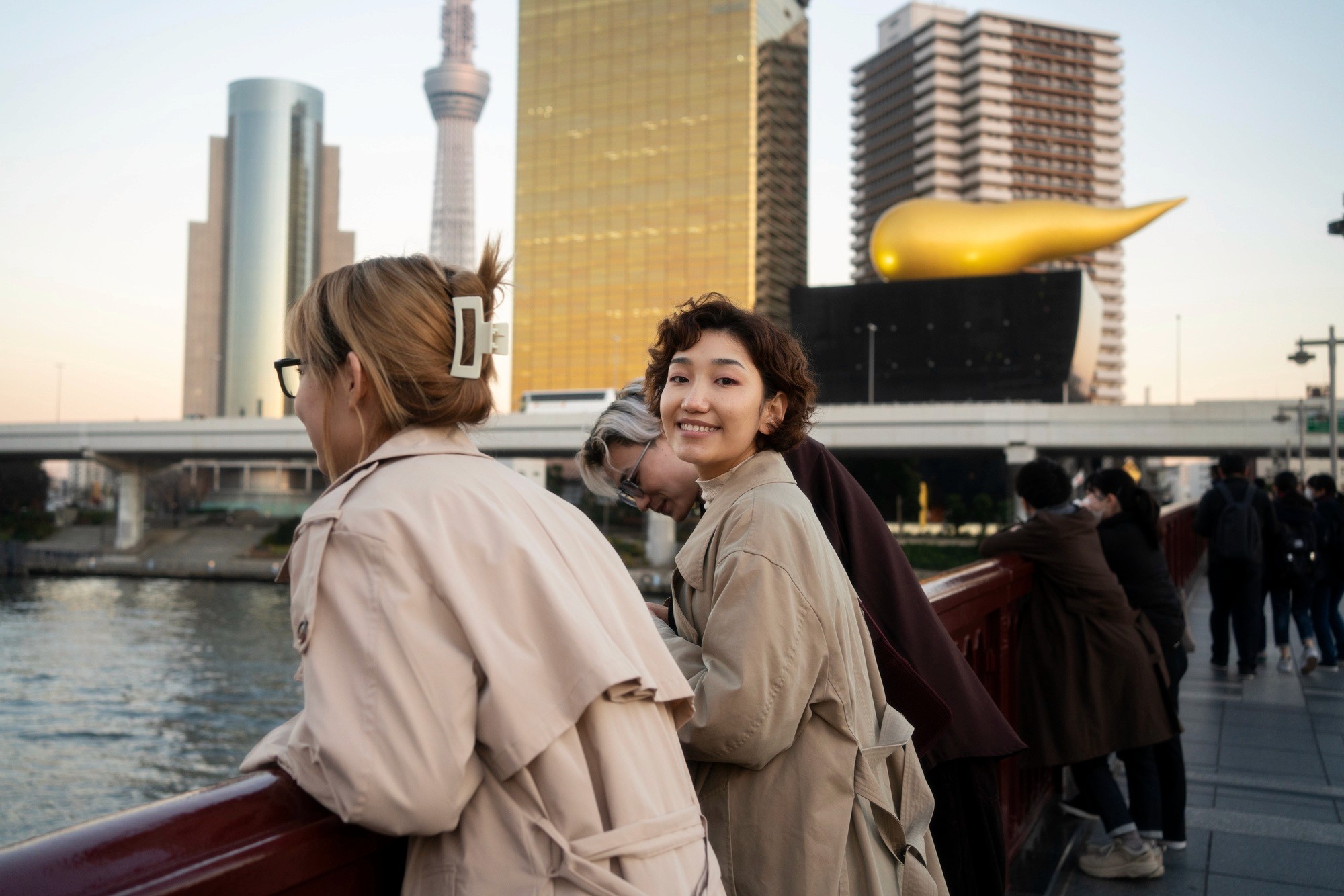 Travelers enjoying the view from a bridge in Asakusa, Tokyo, with the Tokyo Skytree and Asahi Beer Hall golden flame sculpture in the background