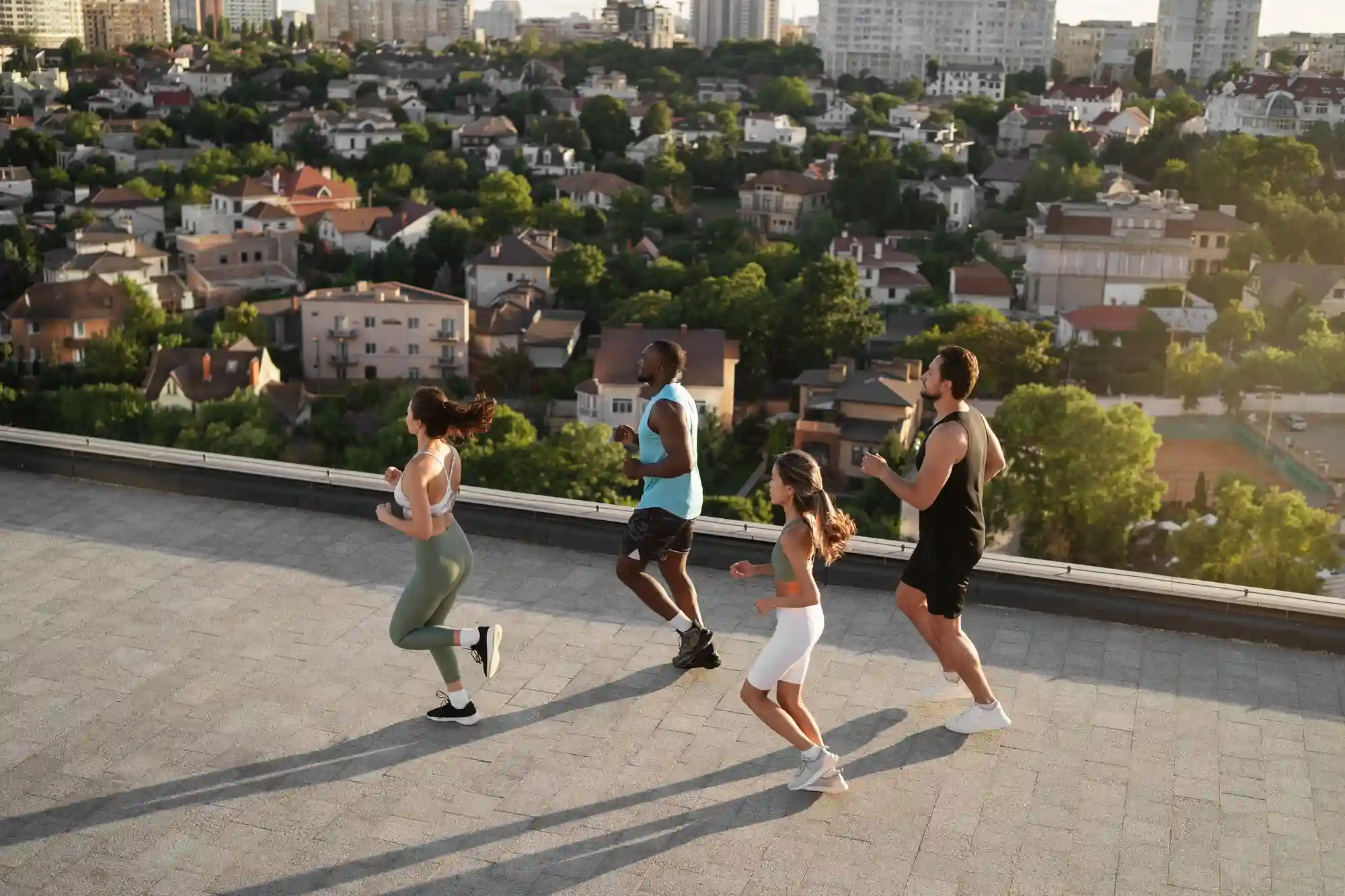 A group of diverse friends jogging together on a scenic urban rooftop during a bright, sunny sunset.