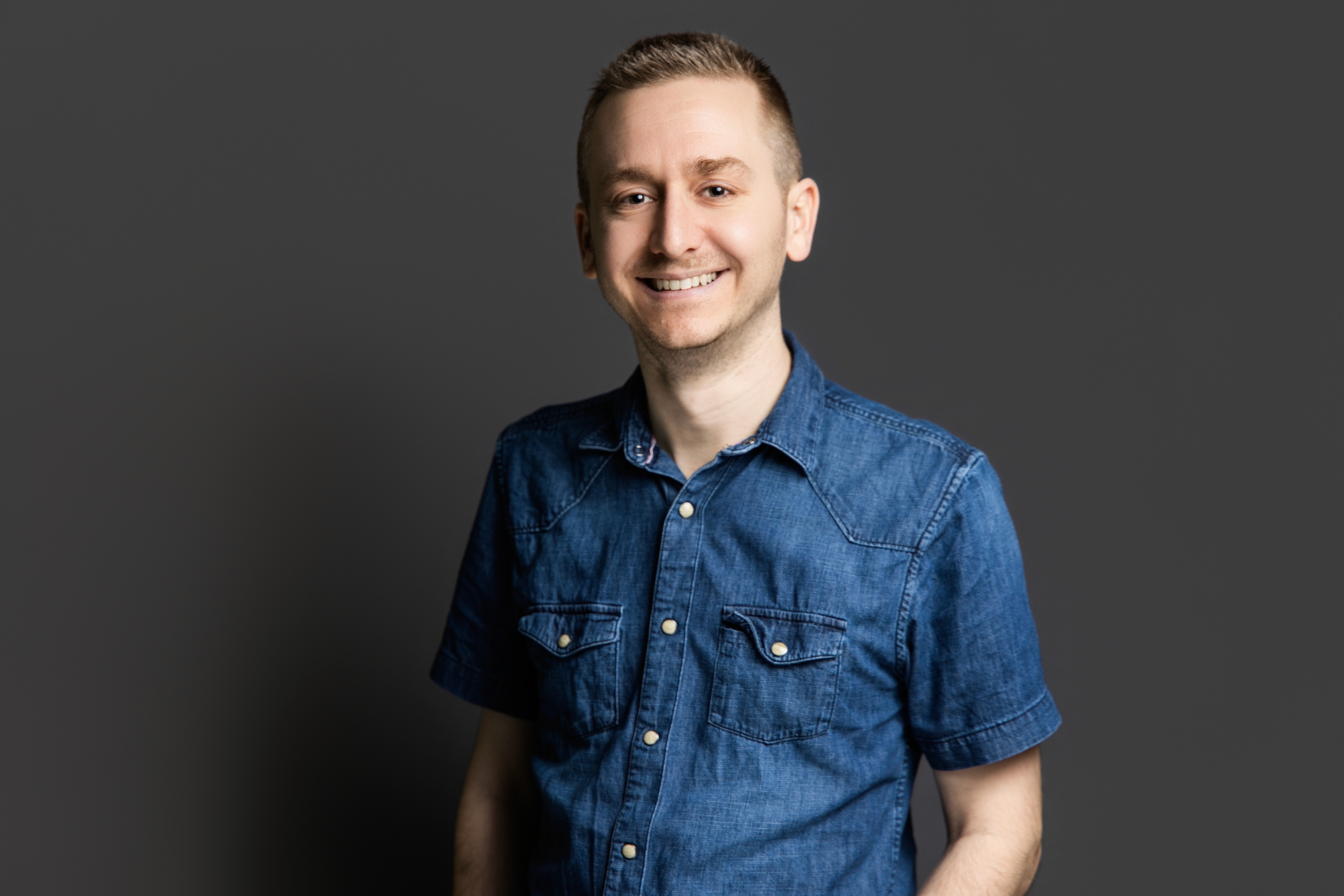 A woman with short curly hair wearing a black t-shirt looks into the camera.