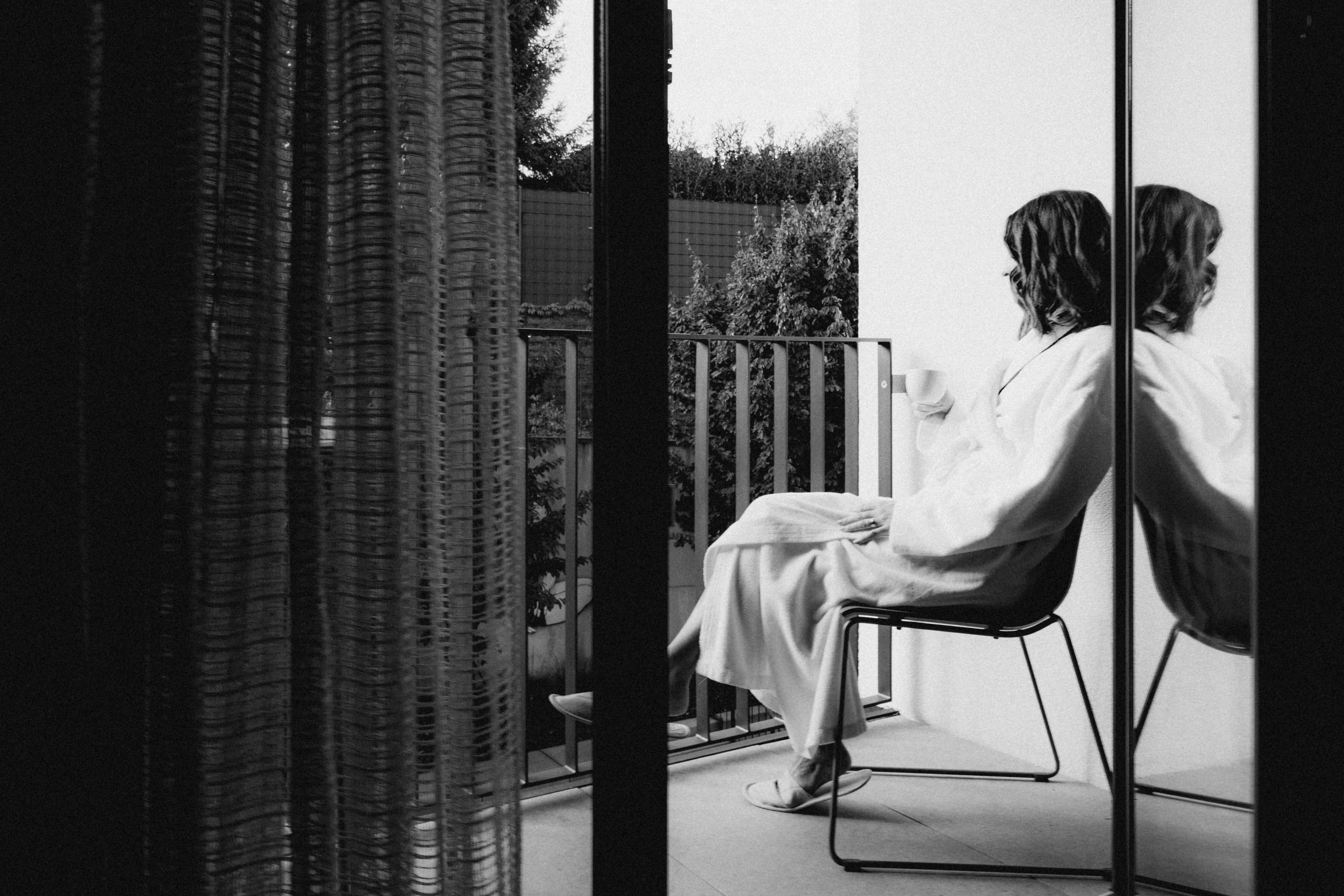 A minimalist interior view featuring a person seated in a chair, reflected in a glass partition.