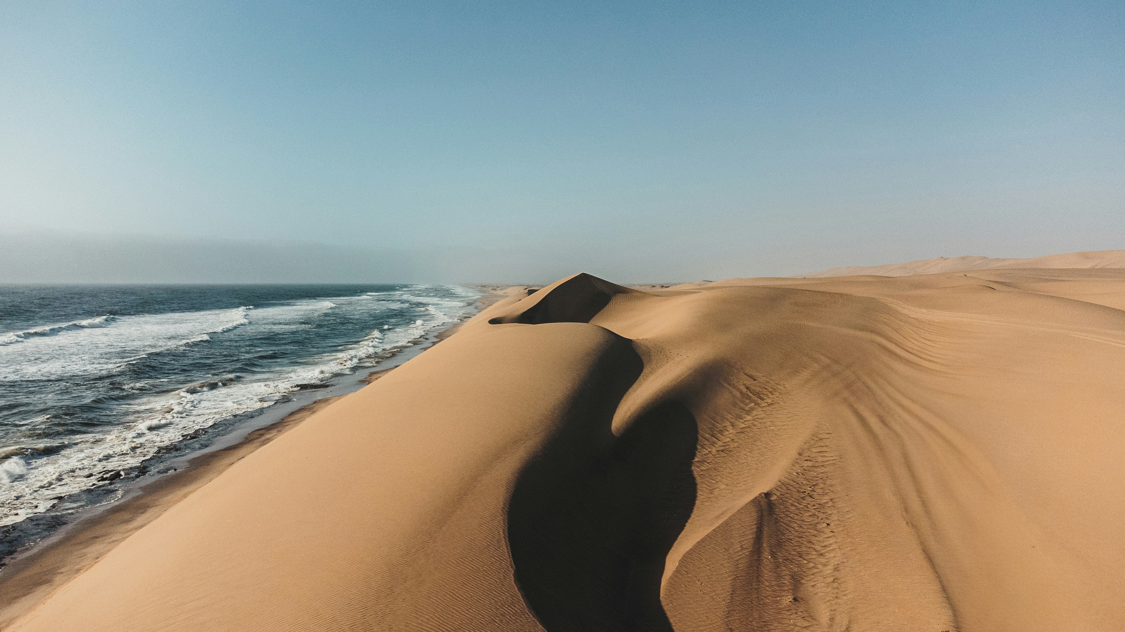 Vast sand dunes meet the ocean under a clear sky