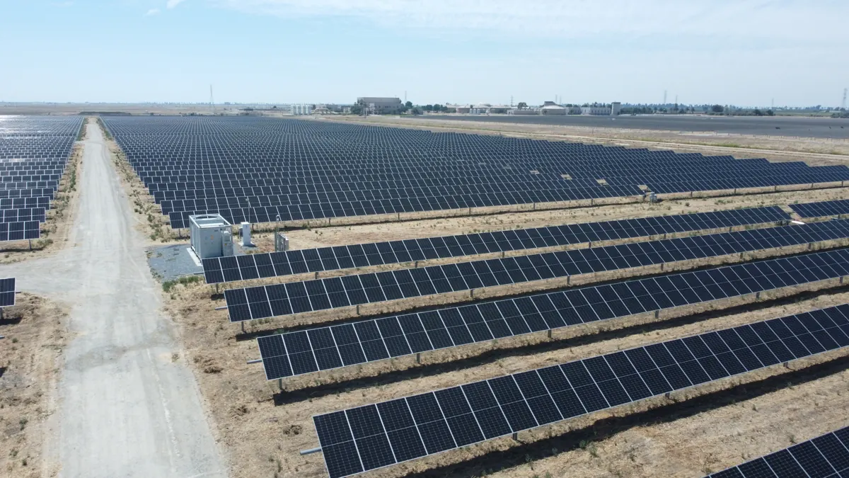 Drone view down a gravel road between ground-mount solar arrays in Fresno, CA