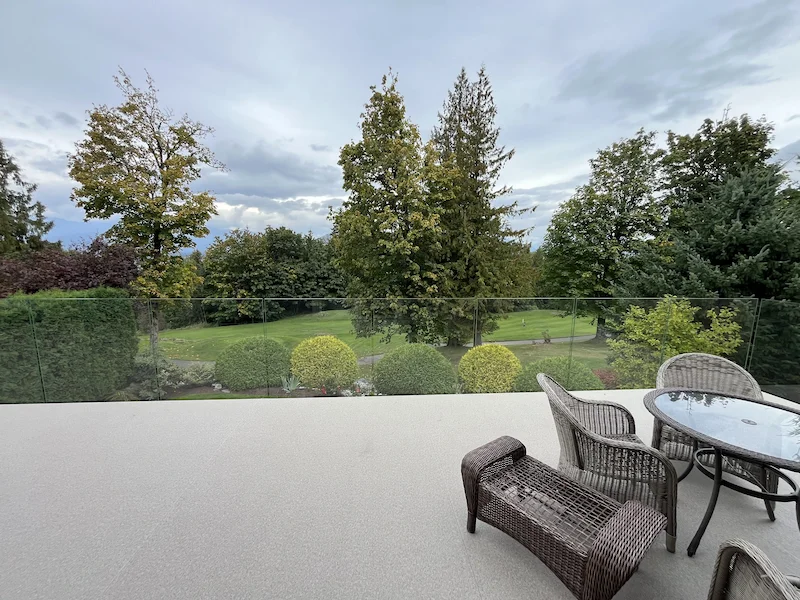 Frameless glass railing on an upper patio overlooking landscaped gardens and mature trees, blending outdoor living with natural views.