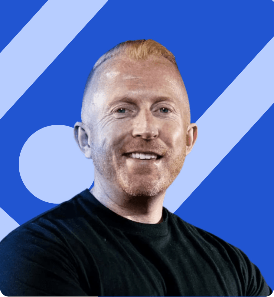 Professional headshot of man with glasses and beard wearing navy suit jacket and white shirt, smiling at camera against blue background with faded cityscape