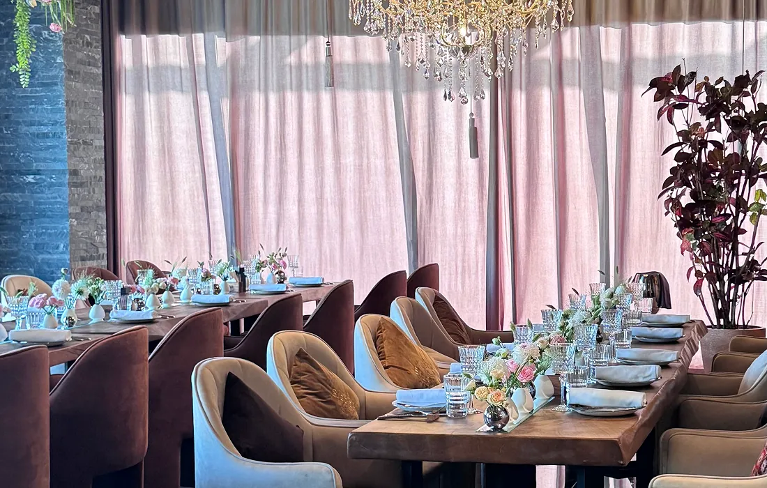 Stylish restaurant interior with long wooden tables, floral centerpieces, and soft pink curtains