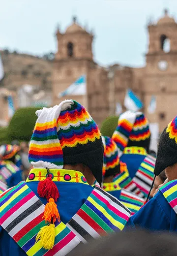 Pessoas com trajes tradicionais andinos coloridos em celebração cultural em praça histórica de Cusco, no Peru