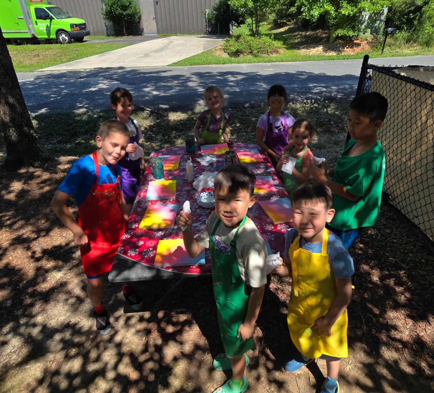 Summer campers working on paintings at an outdoor table under a tree