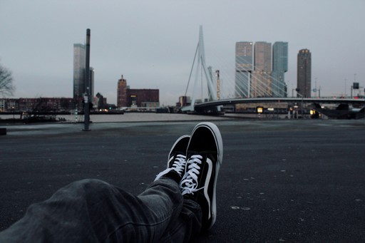 A person's sneaker resting on a rooftop, with a city skyline visible in the background on a cloudy day.