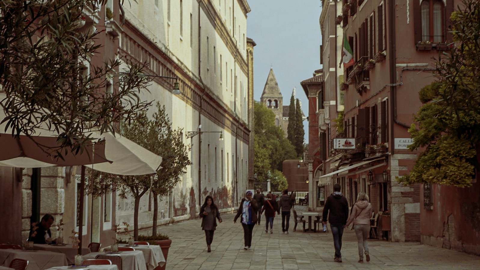 Narrow cobblestone street in Rome lined with historic buildings, cafes, and pedestrians, photographed by Janice Chen.