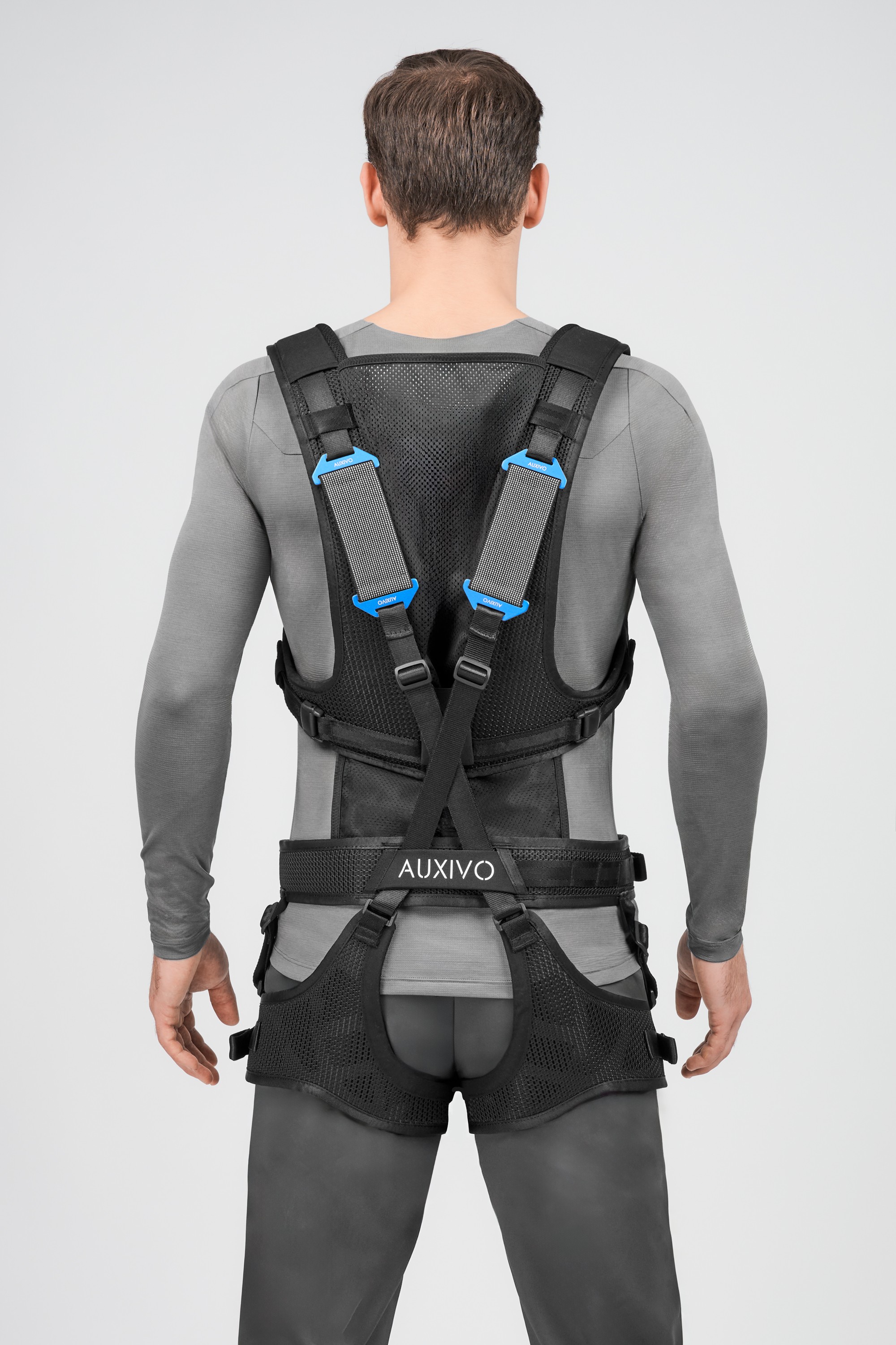 Rear view of the Auxivo LiftSuit exoskeleton worn by a user, showing the ergonomic harness and lumbar support for handling.