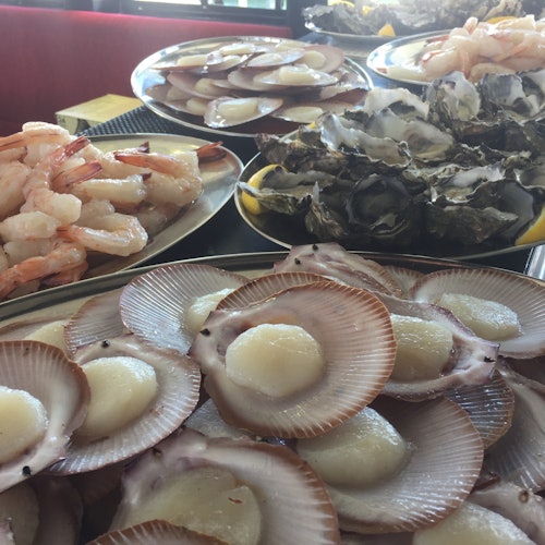 Plates of fresh seafood including scallops, oysters, and shrimp displayed on a table.